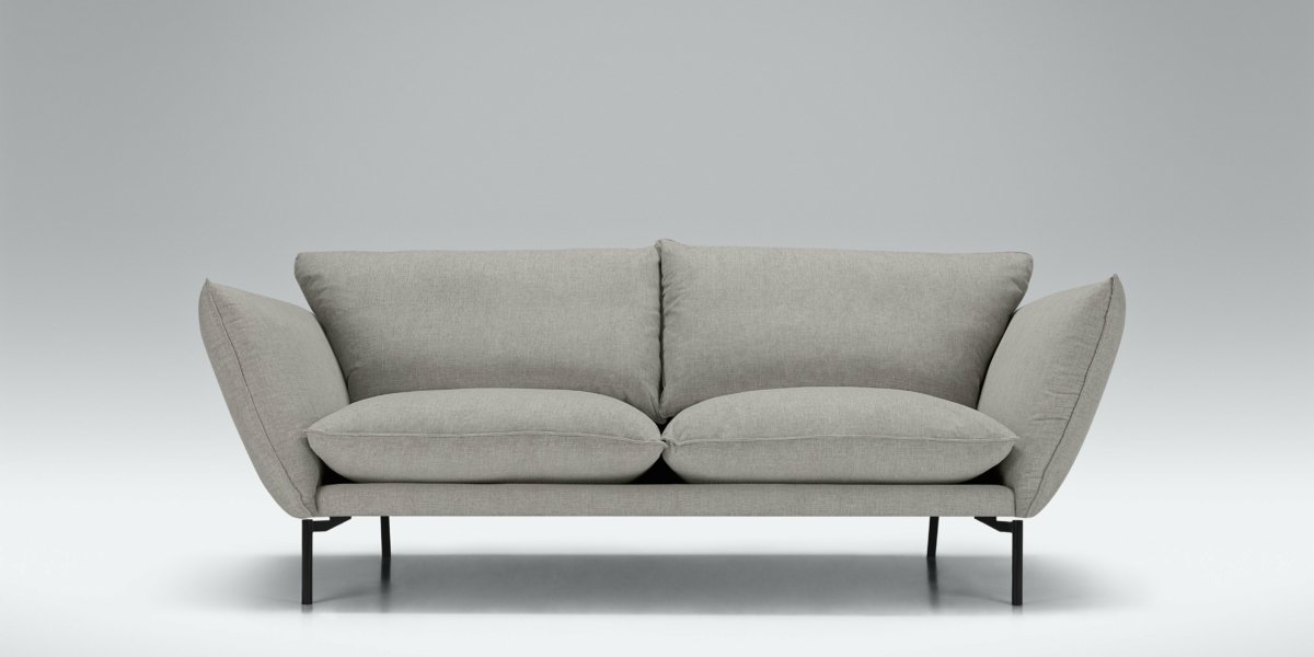 Canapé moderne chic gris avec deux coussins, pieds en métal noir et larges accoudoirs, rappelant le style d'un appartement parisien, sur fond gris clair. Canape Paris by Atelier Bis