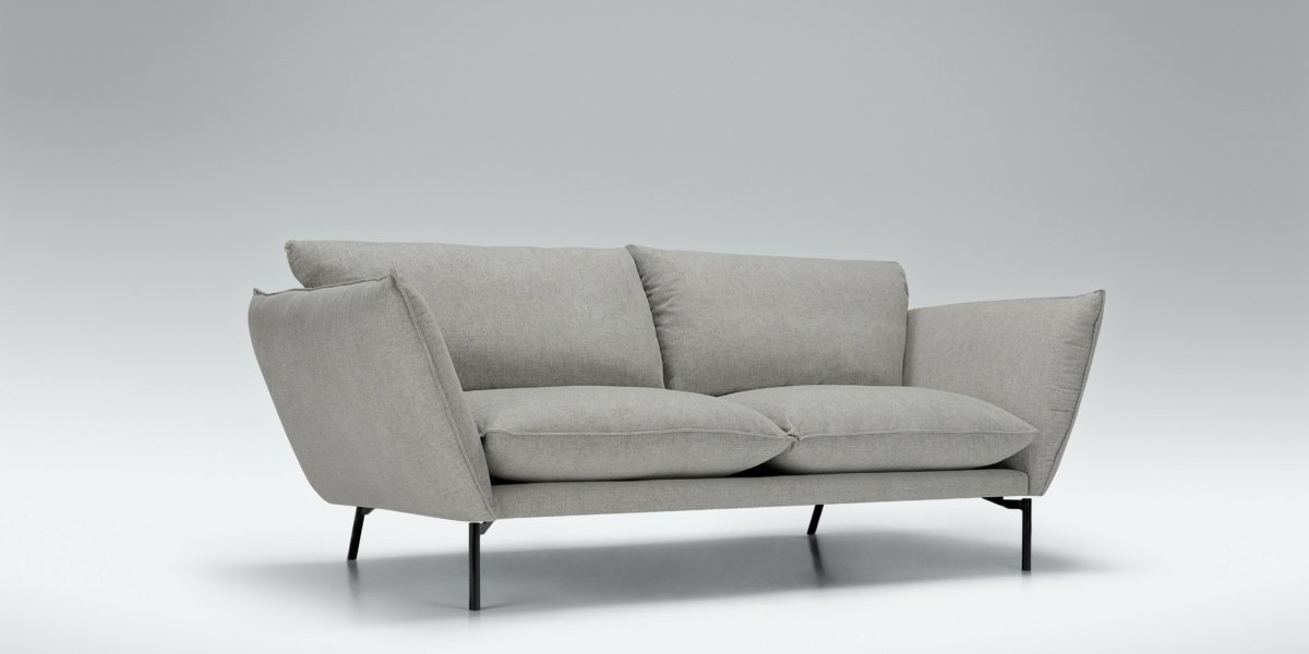 Canapé minimaliste gris avec accoudoirs inclinés et pieds fins noirs sur fond gris clair uni, offrant une touche d'élégance parisienne. Canape Paris by Atelier Bis