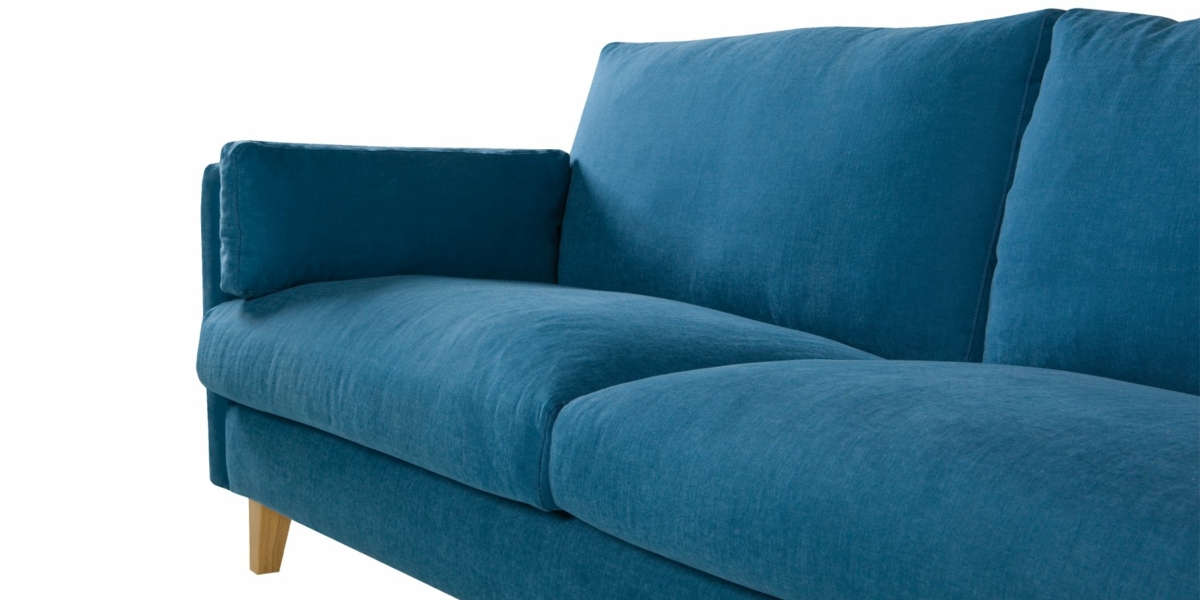 Un canapé bleu chic avec des coussins moelleux et des pieds en bois se dresse élégamment sur un fond blanc. Canape Paris by Atelier Bis