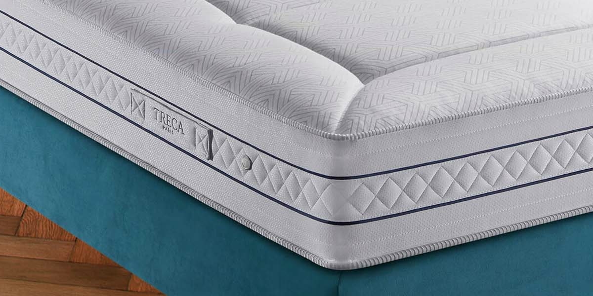 Gros plan d'un matelas blanc aux motifs texturés sur un cadre de lit bleu sarcelle, posé sur un parquet rappelant l'élégance parisienne. Canape Paris by Atelier Bis