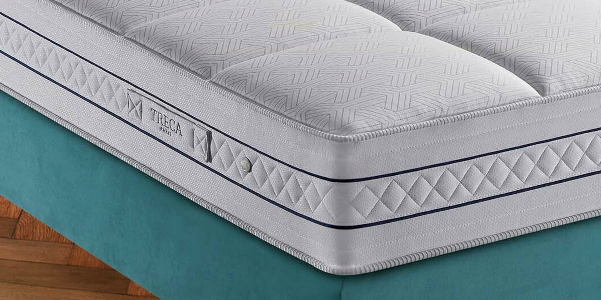 Gros plan d'un matelas soigneusement confectionné avec un motif géométrique sur un cadre de lit bleu sarcelle, rappelant les showrooms parisiens chics. Canape Paris by Atelier Bis