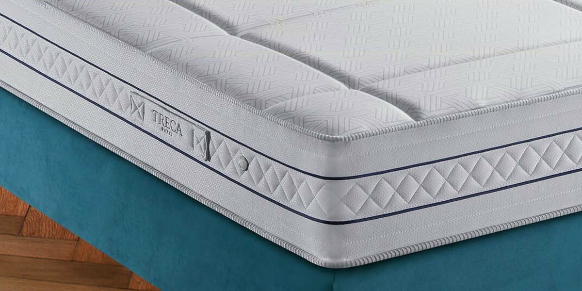 Gros plan d'un matelas de haute qualité avec une housse blanche texturée et une bordure bleue, gracieusement placé sur une base bleu sarcelle comme un canapé exquis, reposant sur un plancher en bois. Canape Paris by Atelier Bis