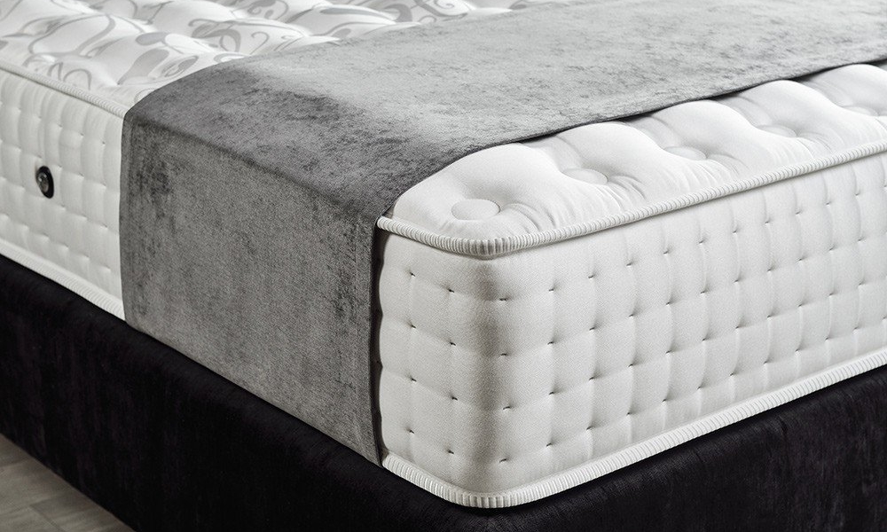 Gros plan sur un matelas épais et matelassé au design gris et blanc, offrant une qualité parisienne, posé sur un cadre de lit foncé. Canape Paris by Atelier Bis