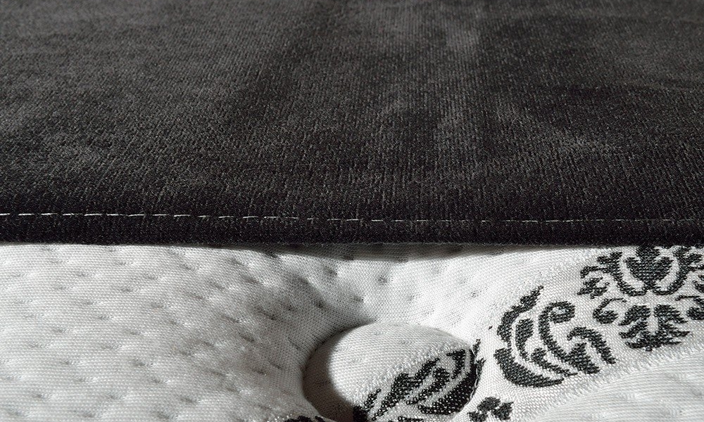 Un gros plan d'un surmatelas gris foncé repose élégamment sur un matelas blanc orné de motifs floraux noirs, offrant un mélange parisien de qualité et de charme. Canape Paris by Atelier Bis