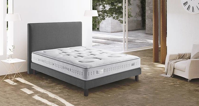 Une chambre moderne avec un lit rembourré gris rappelant un canapé chic, un matelas blanc et une décoration minimaliste qui respire la qualité. Canape Paris by Atelier Bis