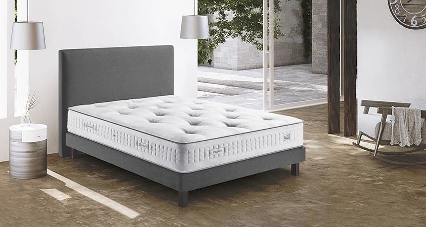 Chambre parisienne moderne avec un lit tapissé gris, un matelas blanc, deux suspensions, une table d'appoint et une horloge ornant le mur - une retraite chic où le style rencontre le confort à tout prix. Canape Paris by Atelier Bis