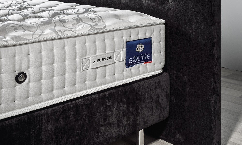 Gros plan d'un matelas blanc capitonné sur un cadre de lit rembourré foncé avec des étiquettes attachées, mettant en valeur la qualité rappelant un canapé parisien chic. Canape Paris by Atelier Bis