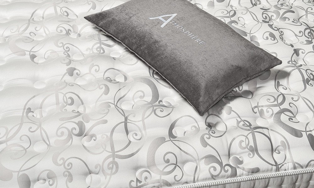 Un matelas gris à motifs tourbillonnants est élégamment orné d'un oreiller gris étiqueté « Atmosphère », rappelant le style parisien chic. Canape Paris by Atelier Bis