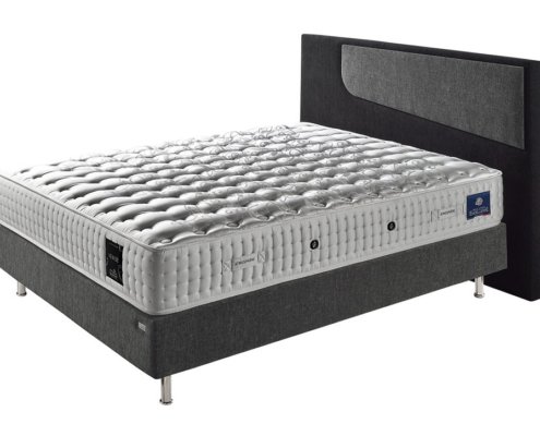 Un lit gris moderne avec un matelas matelassé et une tête de lit en tissu noir, présenté sur un fond blanc, illustrant un savoir-faire de qualité. Canape Paris by Atelier Bis