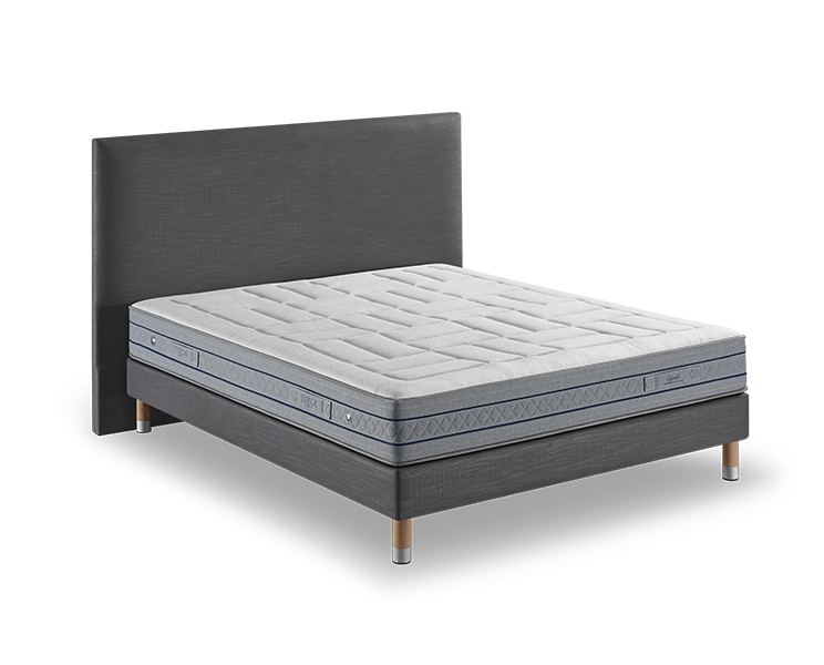 Lit moderne avec tête de lit rembourrée et base grise, avec matelas blanc capitonné sur pieds en bois. Ce meuble offre une qualité digne d'un canapé luxueux, assurant à la fois style et confort dans n'importe quelle chambre à coucher. Canape Paris by Atelier Bis