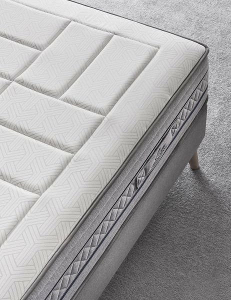 Gros plan d'un matelas moderne aux motifs géométriques, posé sur un canapé capitonné gris qui respire l'élégance parisienne, le tout sur un tapis gris clair. Canape Paris by Atelier Bis