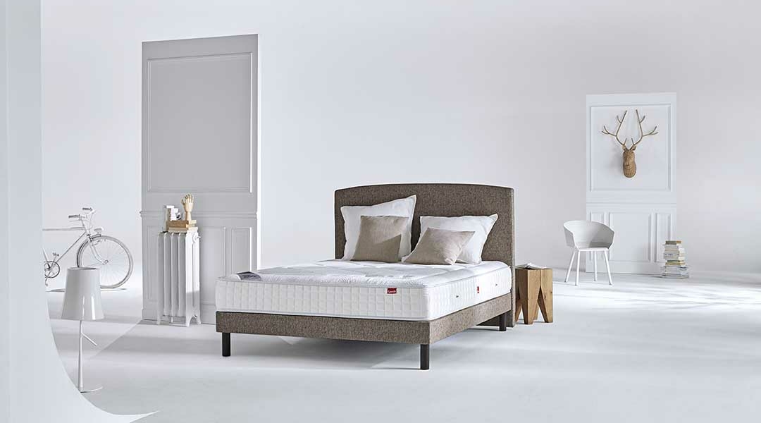 Chambre minimaliste dans un décor blanc parisien comprenant un lit avec des oreillers, un vélo élégant et une tête de cerf décorative sur le mur, le tout dégageant un air de qualité. Canape Paris by Atelier Bis