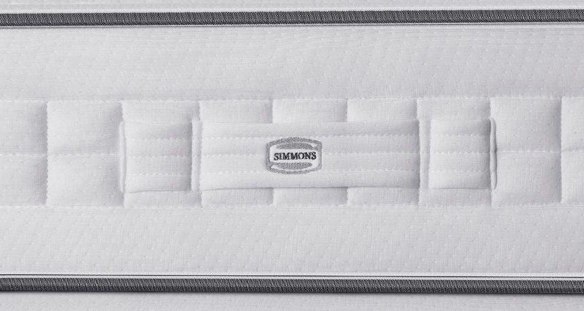 Gros plan sur un matelas blanc avec un motif surpiqué, mettant en valeur un logo gris foncé au centre. Ce mélange de qualité et de style pourrait facilement être trouvé dans les maisons parisiennes les plus chics, où le prix rencontre le goût du haut de gamme. Canape Paris by Atelier Bis