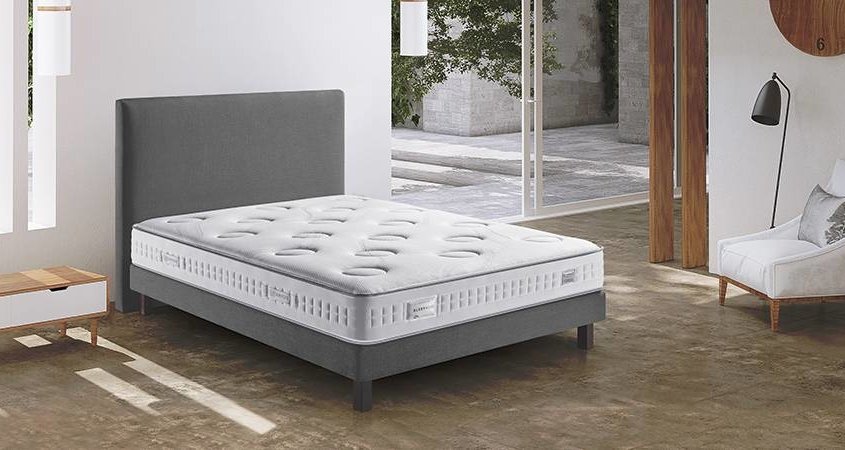 Chambre moderne avec lit et matelas gris, table d'appoint en bois et lumière naturelle qui entre, faisant écho à l'élégance intemporelle d'une escapade parisienne. La chambre incarne la qualité avec chaque détail soigneusement choisi. Canape Paris by Atelier Bis