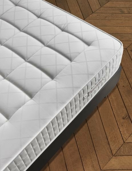 Matelas matelassé blanc sur un sol en bois à chevrons, offrant une qualité inégalée qui évoque le charme de Paris. Canape Paris by Atelier Bis