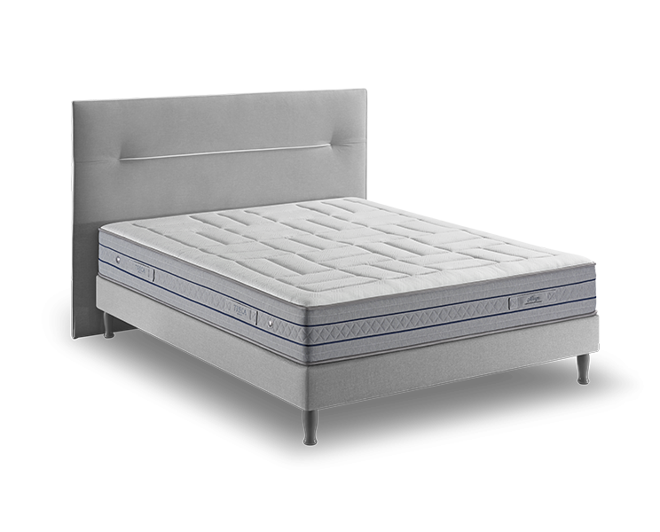 Lit rembourré gris avec un matelas et une tête de lit matelassés, mettant en valeur des pieds en métal et des accents bleus, reflétant la sophistication chic du style parisien. Canape Paris by Atelier Bis