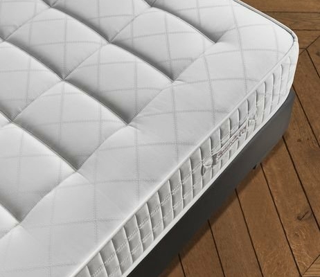 Un matelas blanc au motif matelassé repose sur un cadre de lit sombre, dégageant un air de qualité parisienne tout en complétant le parquet à chevrons. Canape Paris by Atelier Bis