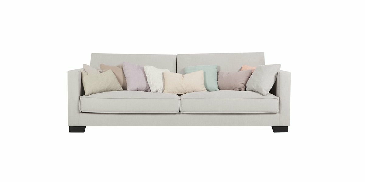 Un canapé gris clair orné de plusieurs coussins aux couleurs pastel sur un fond blanc immaculé, offrant à la fois qualité et style. Canape Paris by Atelier Bis