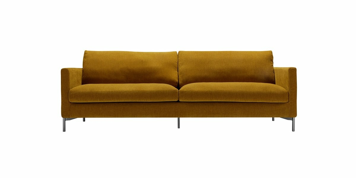Un canapé jaune moutarde avec deux coussins et des pieds en métal élégants, vu de face sur un fond blanc, prêt à briller dans n'importe quelle salle d'exposition. Canape Paris by Atelier Bis