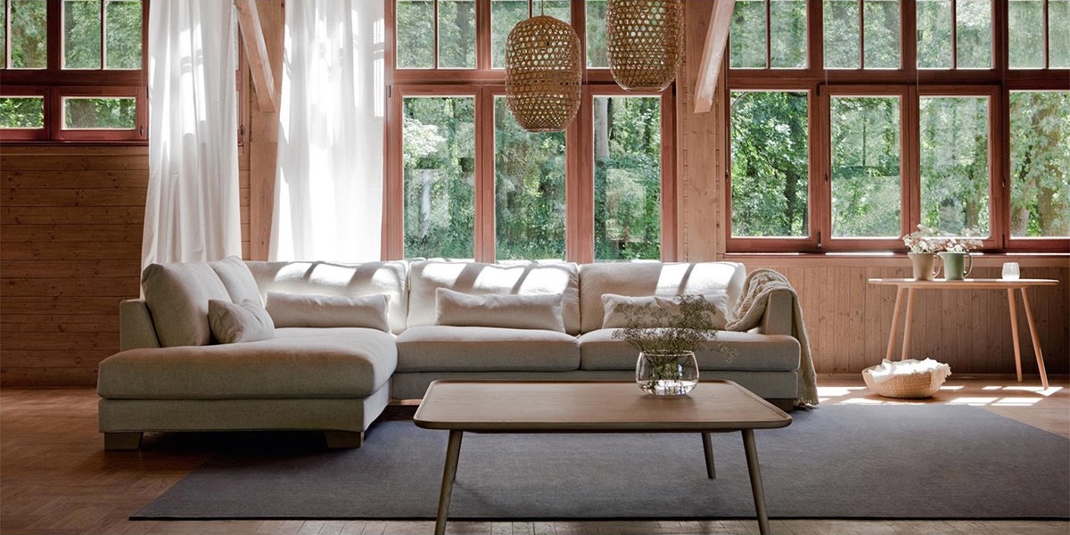 Salon lumineux avec un canapé beige, une table basse en bois et de grandes fenêtres inondant l'espace de lumière, dégageant cette touche parisienne de qualité. Canape Paris by Atelier Bis