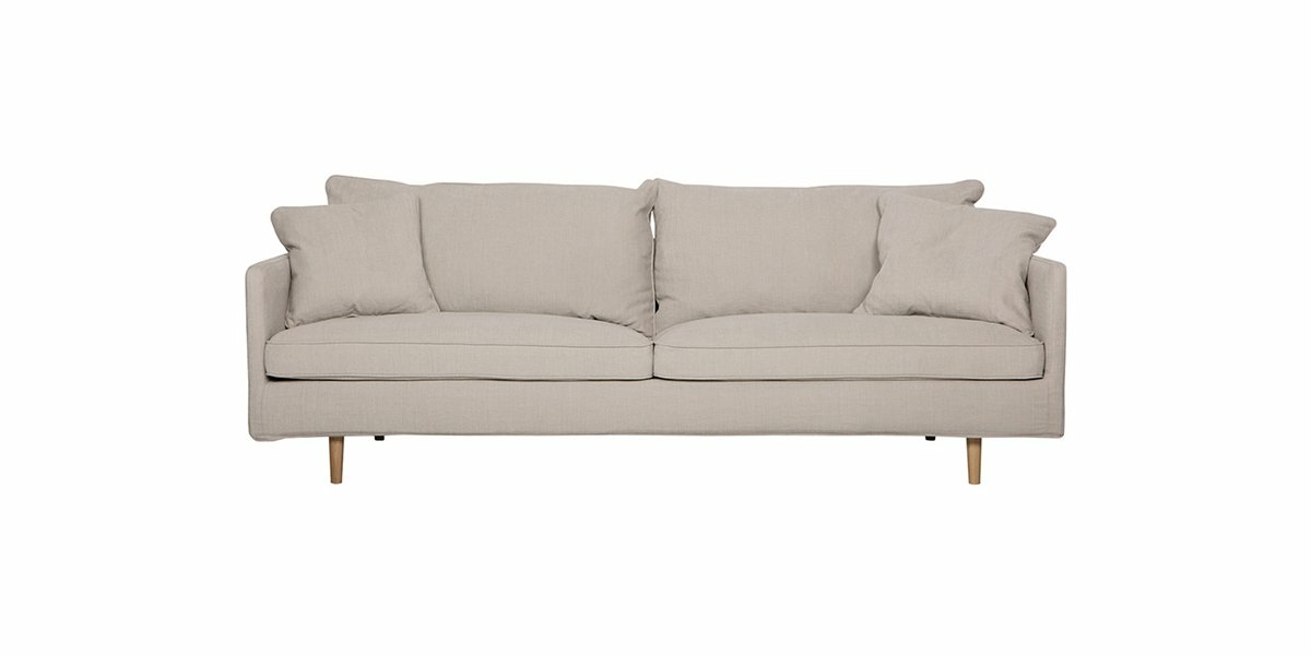 Un canapé beige trois places avec quatre coussins et des pieds en bois respire la qualité, présenté avec élégance sur un fond blanc uni dans un showroom parisien chic. Canape Paris by Atelier Bis