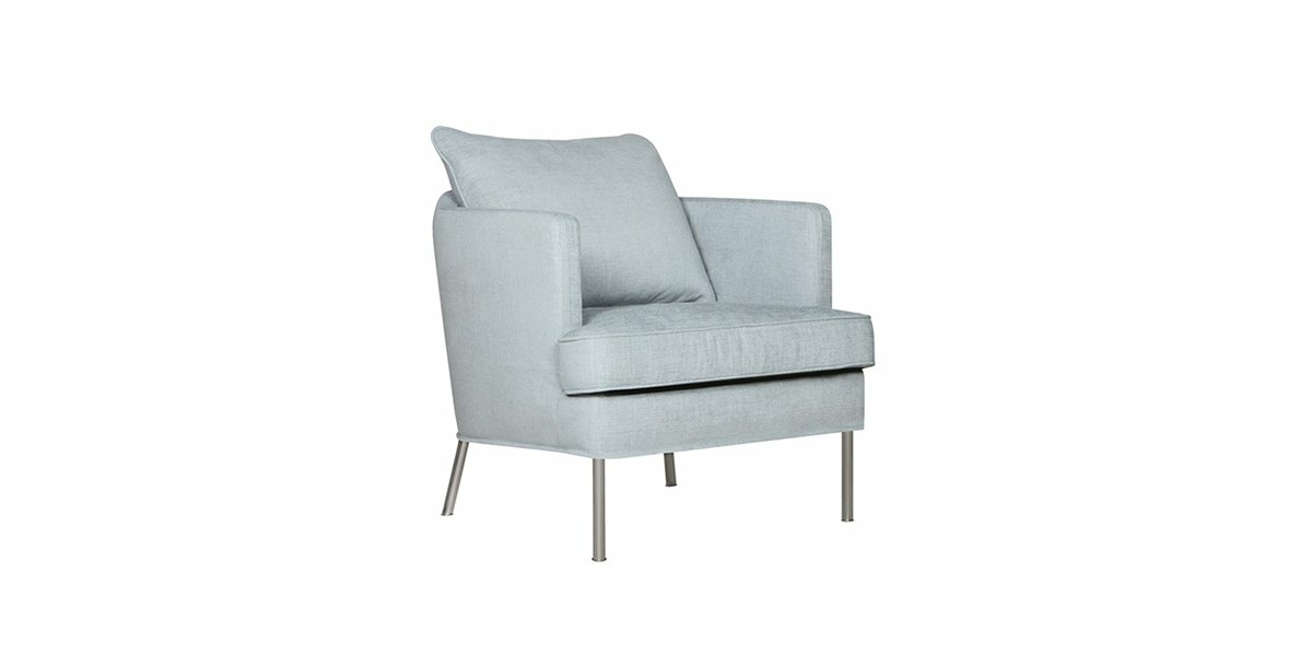 Dans un décor de showroom, ce fauteuil gris clair avec coussin et pieds métalliques est positionné avec goût en angle sur un fond blanc immaculé. Canape Paris by Atelier Bis