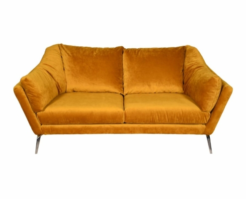 Un canapé deux places en velours jaune moutarde, rappelant une pièce d'exposition parisienne chic, présente des accoudoirs inclinés et des pieds en métal minces sur un fond blanc immaculé. Canape Paris by Atelier Bis