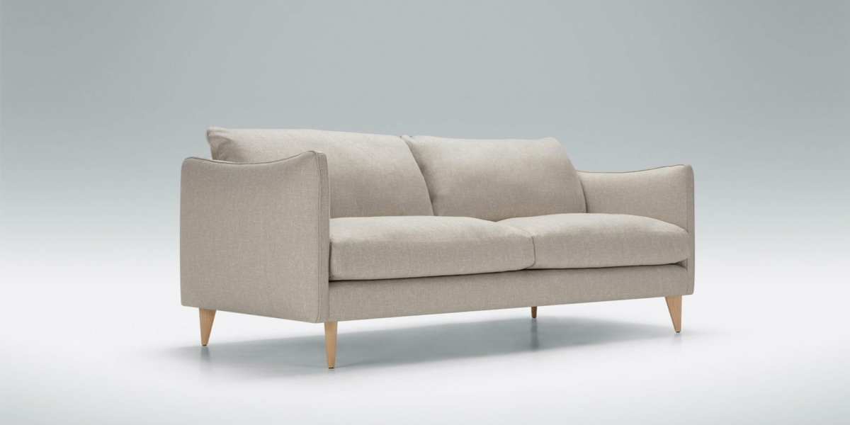 Un canapé beige aux pieds en bois agrémente ce showroom minimaliste, offrant une touche de qualité au cœur de Paris. Canape Paris by Atelier Bis