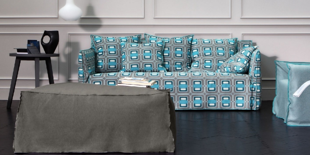 Entrez dans cette salle d'exposition élégante comprenant un canapé à motifs bleus, complété par un pouf gris, une élégante table d'appoint noire et une élégante suspension blanche. Canape Paris by Atelier Bis