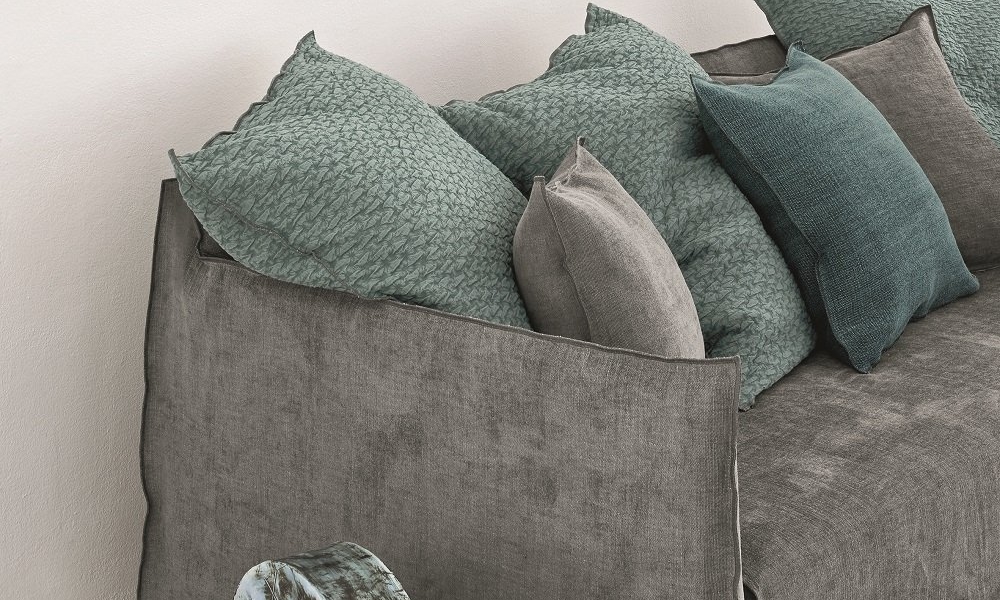 Salon contemporain présentant une esthétique de qualité showroom avec un canapé gris, des coussins bleu sarcelle, une décoration murale en céramique et une pièce d'accent ronde bleue sur le sol. Canape Paris by Atelier Bis