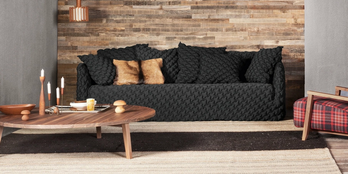 Chambre cosy avec un canapé texturé noir, une table basse en bois et un fauteuil à carreaux, le tout adossé à un mur d'accent en bois chic, rappelant un showroom parisien. Canape Paris by Atelier Bis