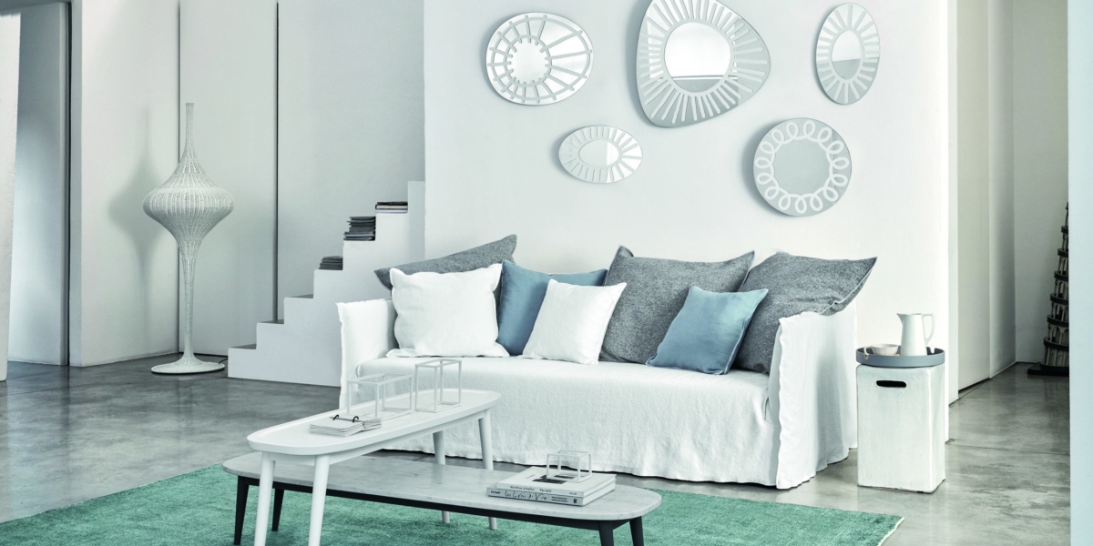 Salon moderne avec un canapé doté d'un revêtement blanc, de coussins gris et bleus, de miroirs décoratifs et de tables gigognes sur un tapis vert - un mélange exquis de style et de confort avec un rapport qualité-prix inégalé. Canape Paris by Atelier Bis