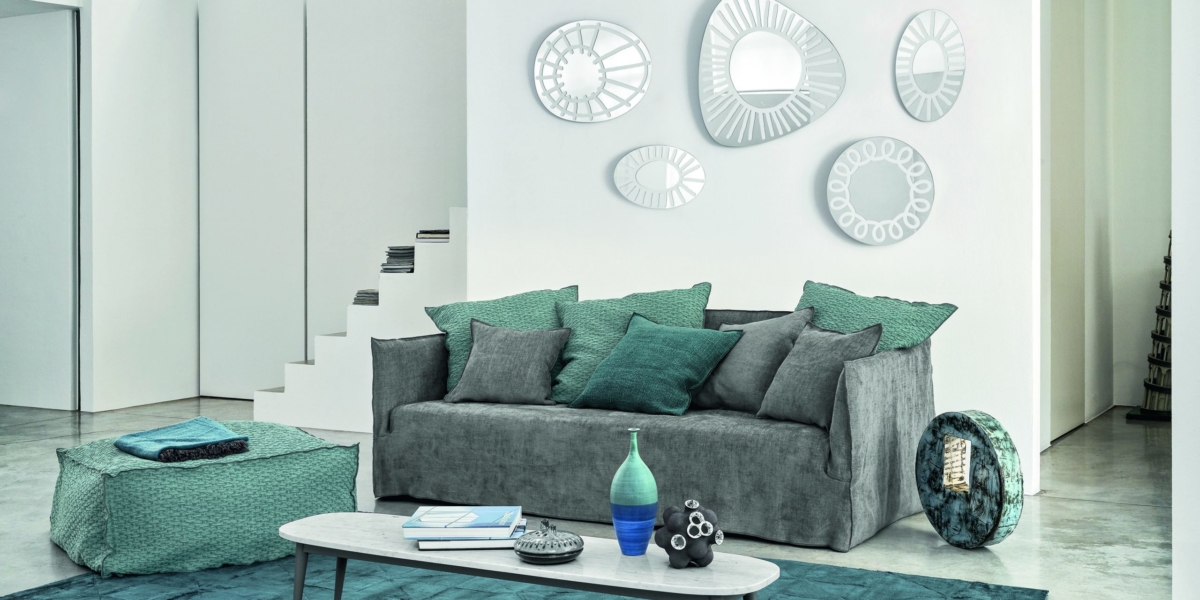 Salon moderne présentant la qualité d'une salle d'exposition, avec un canapé gris orné de coussins bleu sarcelle, une œuvre d'art murale abstraite, une table basse élégante et un tapis bleu sarcelle sur le sol en béton. Canape Paris by Atelier Bis