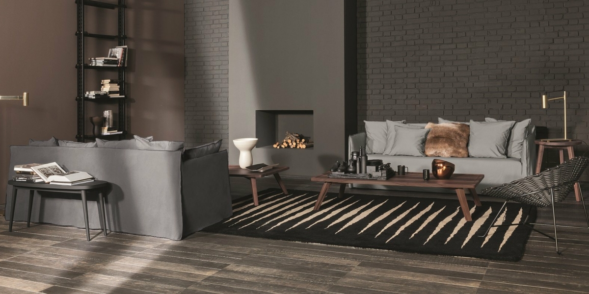 Salon élégant avec canapé gris, mur de briques noires, décoration moderne et cheminée intégrée, offrant une qualité luxueuse à un prix imbattable. Canape Paris by Atelier Bis