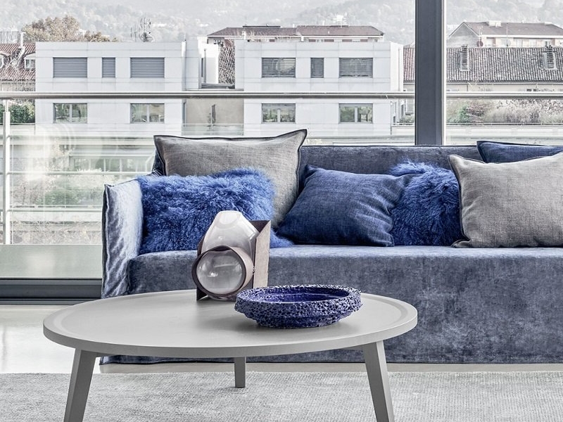 Découvrez un salon parisien moderne avec une table basse grise chic, des objets de décoration élégants et un canapé bleu moelleux. De grandes fenêtres offrent une vue imprenable sur le paysage urbain, alliant sophistication et charme chaleureux. Canape Paris by Atelier Bis