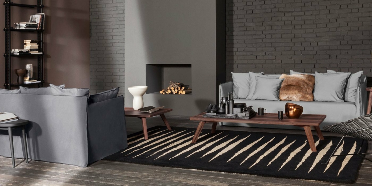 Salon moderne avec canapés gris, tables en bois, mur de briques, cheminée et tapis rayé, dégageant un charme parisien. Canape Paris by Atelier Bis