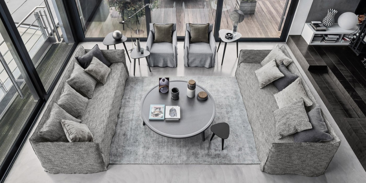 Un salon chic et moderne avec deux canapés gris, des fauteuils moelleux et une table basse ronde, encadrés par de grandes fenêtres offrant une vue enchanteresse sur la terrasse. Parfait pour savourer une touche d'élégance parisienne. Canape Paris by Atelier Bis