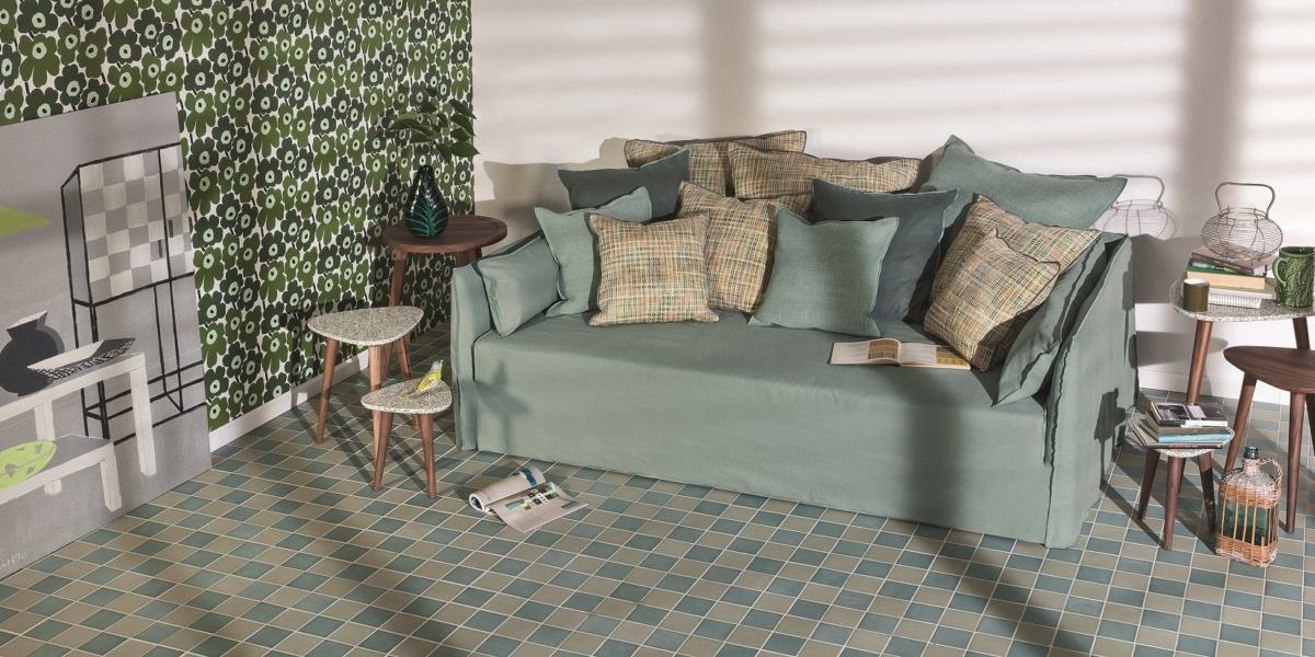 Chambre cosy à Paris avec un canapé vert moelleux, des coussins à motifs, des tables d'appoint et des objets décoratifs contre des murs géométriques et un sol carrelé. Canape Paris by Atelier Bis