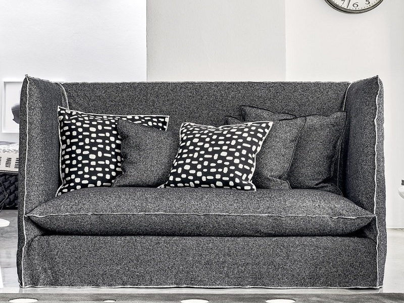 Un élégant canapé gris, orné de coussins à motifs noirs et blancs, orne cette pièce moderne rappelant un showroom parisien, avec une élégante horloge murale. Canape Paris by Atelier Bis