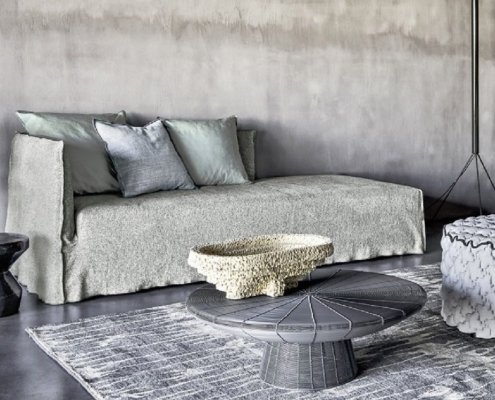 Salon moderne avec un canapé gris, des tables grises, un pouf tissé, un bol décoratif et un tapis texturé qui évoquent l'élégance chic d'un showroom parisien. Canape Paris by Atelier Bis