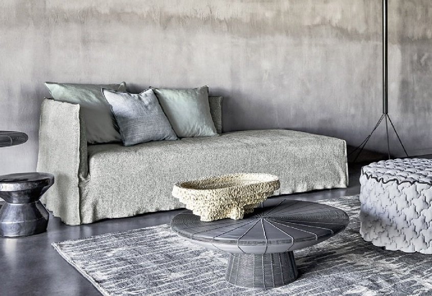 Salon moderne avec un canapé gris, des tables grises, un pouf tissé, un bol décoratif et un tapis texturé qui évoquent l'élégance chic d'un showroom parisien. Canape Paris by Atelier Bis