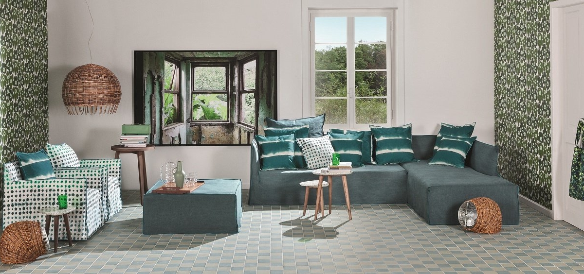 Découvrez un salon d'inspiration parisienne avec une décoration verte et blanche, des murs à motifs et un grand canapé. Des tentures tissées et un tableau sur le thème de la nature créent une atmosphère chaleureuse rappelant un showroom élégant. Canape Paris by Atelier Bis