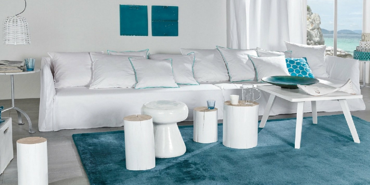 Salon moderne avec canapé blanc de haute qualité, complété par un tapis turquoise et des touches de bleu. Une vue imprenable sur la côte rappelant une retraite parisienne est visible à travers la fenêtre. Canape Paris by Atelier Bis