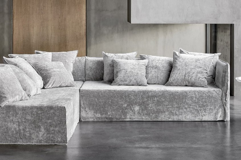 Un canapé sectionnel gris moderne avec des coussins moelleux dans un salon minimaliste évoque l'élégance d'un showroom parisien, complété par une petite table ronde en métal. Canape Paris by Atelier Bis