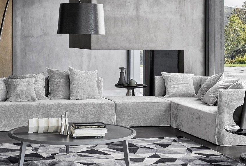 Un salon moderne au style parisien minimaliste comprend un canapé sectionnel gris, un tapis géométrique et une table basse ronde, alliant sans effort élégance et qualité. Canape Paris by Atelier Bis