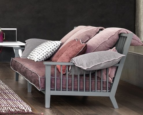 Découvrez notre canapé moderne, présenté dans notre showroom, composé de multiples coussins aux tons de rose et de gris sur un plancher en bois, accompagné d'une table d'appoint chic. Faites l'expérience d'une qualité et d'un style inégalés qui offrent un excellent rapport qualité-prix. Canape Paris by Atelier Bis