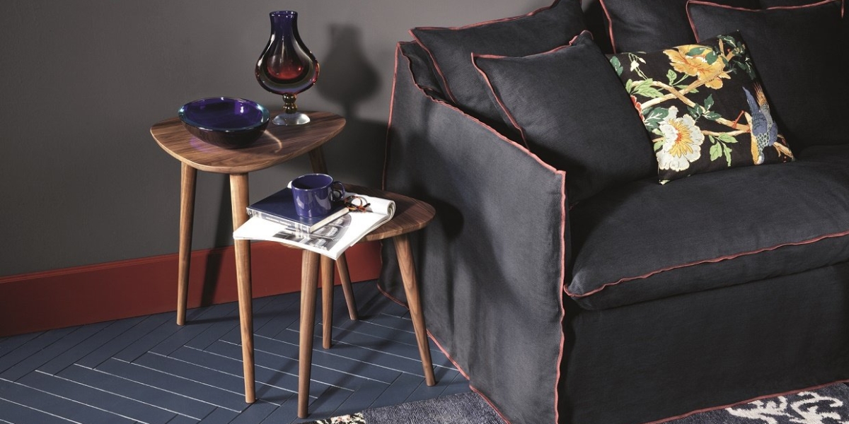 Découvrez l'élégance d'un showroom parisien dans ce salon cosy, doté d'un canapé sombre orné de coussins colorés, de tables gigognes et d'un vase chic à côté d'une tasse bleue sur un tapis à motifs. Profitez d'une qualité inégalée dans chaque détail de cet espace élégant. Canape Paris by Atelier Bis