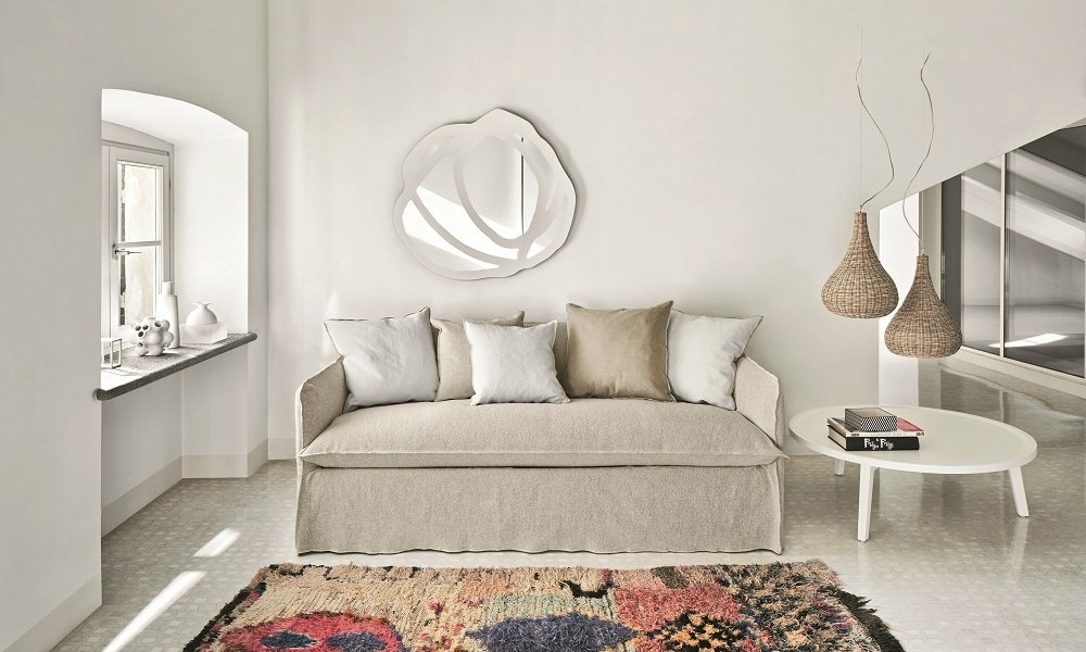 Un salon minimaliste ressemblant à un showroom parisien, avec un canapé beige, un tapis coloré, des suspensions tissées et des œuvres d'art murales modernes. Canape Paris by Atelier Bis