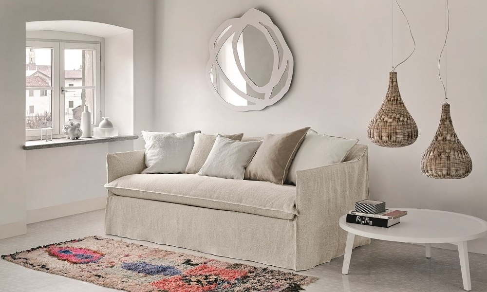 Une touche parisienne chic orne le salon minimaliste avec un canapé beige, des œuvres d'art murales abstraites et des luminaires suspendus en osier, le tout conçu pour la qualité. Le tapis à motifs colorés ajoute du dynamisme à cet espace élégant. Canape Paris by Atelier Bis