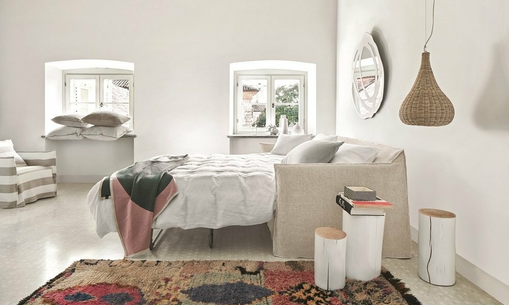 Une chambre minimaliste à Paris comprend un lit douillet, une suspension en osier et un tapis coloré. Les murs blancs se marient à merveille avec la lumière naturelle qui pénètre par les fenêtres, offrant une simplicité élégante à tous les prix. Canape Paris by Atelier Bis